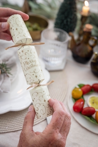 Hands holding Christmas bon-bon at table - Australian Stock Image