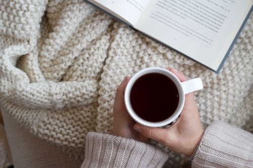 Hands holding coffee mug with woollen blanket and book