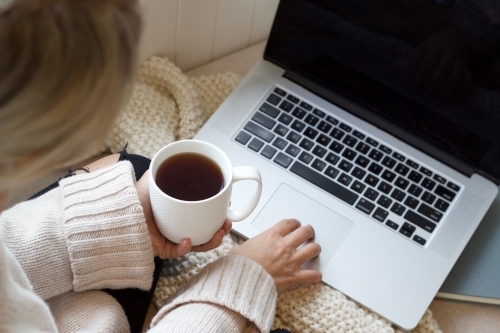 Hands holding coffee mug with woollen blanket and laptop computer and book