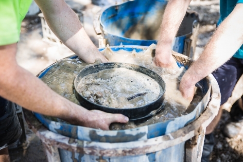 Hands in muddy water of fossicking drum holding sieve