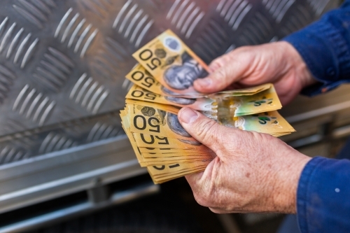 Hands of a handyman counting cash beside tradie ute - Australian Stock Image