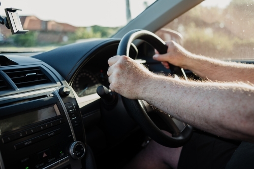 Hands of an anonymous male adult on the steering wheel seen from inside the car - Australian Stock Image