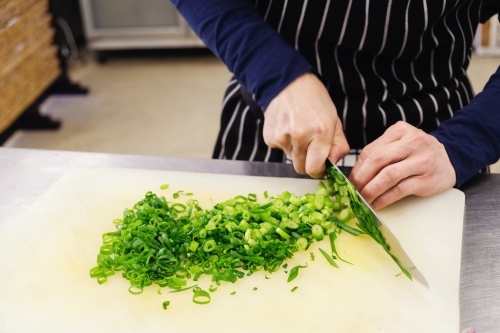 Hands of chef chopping spring onion in the kitchen - Australian Stock Image