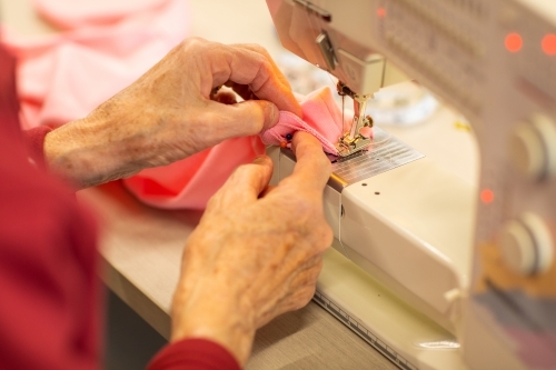 hands of elderly lady guiding fabric through sewing machine - Australian Stock Image