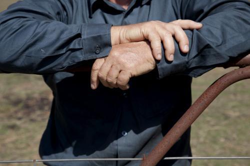 Hands of middle aged male farmer leaning on fence on rural property - Australian Stock Image