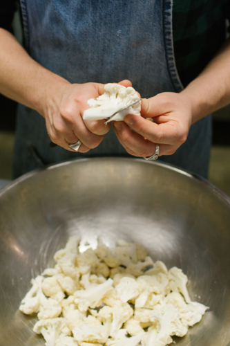 Hands slicing cauliflower in kitchen over metal bowl - Australian Stock Image
