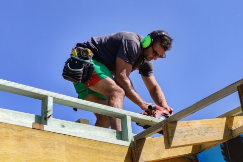 Handsome young builder working with circular saw on timber framing on building site - Australian Stock Image