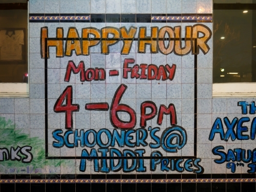Handwritten "Happy Hour" sign on tiles outside a pub