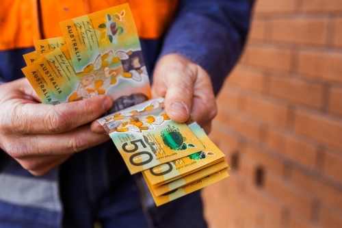Handyman holding bank notes counting cash received as payment for job completion - Australian Stock Image