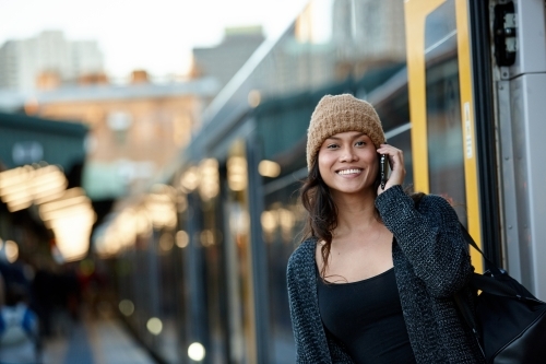 Happy Asian woman getting off train talking on mobile phone - Australian Stock Image