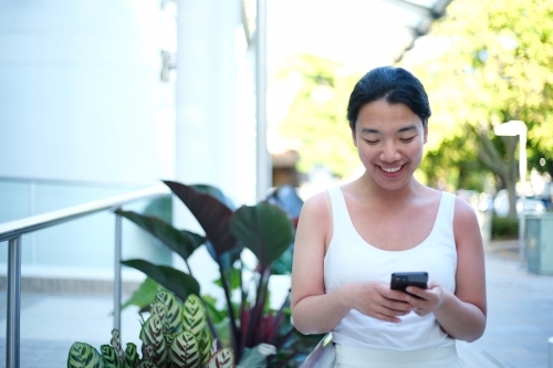 Happy Asian woman holding her mobile phone - Australian Stock Image