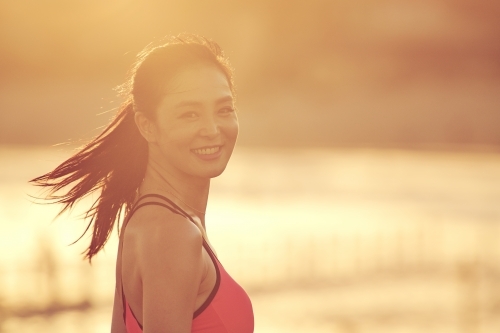 Happy Asian woman looking over shoulder with golden light flare - Australian Stock Image