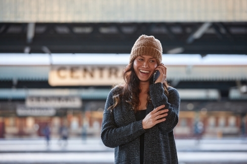 Happy Asian woman talking on mobile whilst waiting at train station - Australian Stock Image