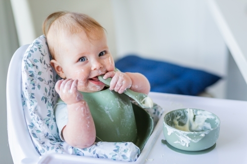 Happy australian baby in high chair eating yoghurt breakfast in high chair - Australian Stock Image