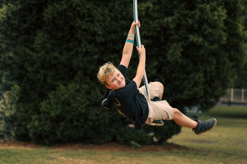 Happy boy playing on swing at playground - Australian Stock Image