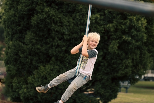 Happy boy playing on swing at playground - Australian Stock Image