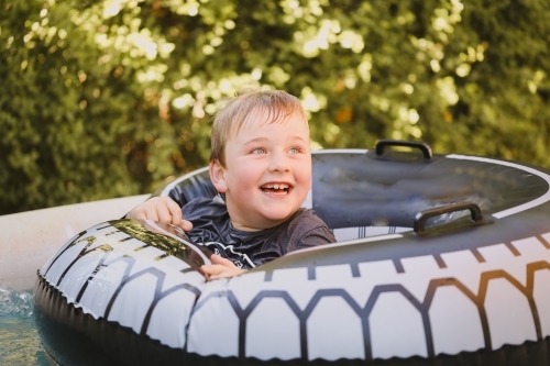 Happy boy swimming with inflatable tyre in backyard pool - Australian Stock Image