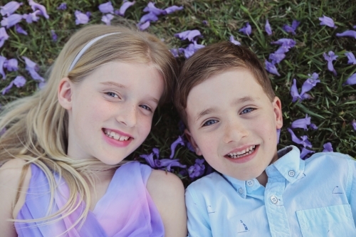 Happy brother and big sister lying on grass in the park - Australian Stock Image