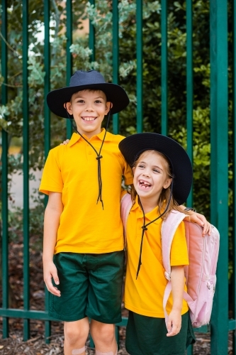 Happy brother and sister laugh and hug beside school fence outside