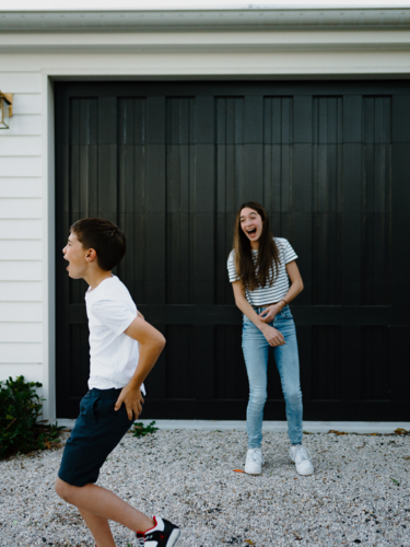 Happy brother and teen sister being silly together outside carport at home - Australian Stock Image