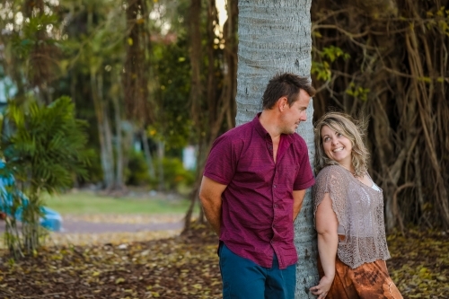Happy couple leaning against palm tree at the park - Australian Stock Image