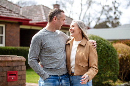 Happy couple standing arm-in-arm looking at each other in the front yard - Australian Stock Image