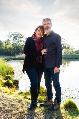 Happy couple standing together by dam in paddock - Australian Stock Image