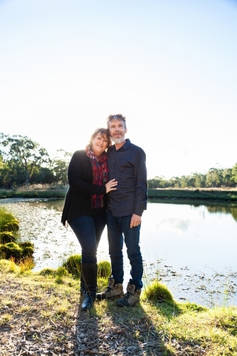 Happy couple standing together by dam in paddock - Australian Stock Image