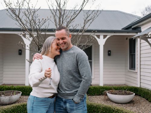 Happy couple stands in the front yard holding a key of their new home - Australian Stock Image