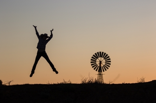Happy cowgirl jumping and windmill in silhouette - Australian Stock Image