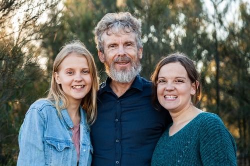 Happy dad with his two teenage daughters hug together outside - Australian Stock Image