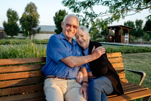 Happy, elderly retired married couple hugging on a park bench