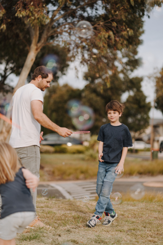 Happy family blowing and playing with bubbles in their yard. - Australian Stock Image