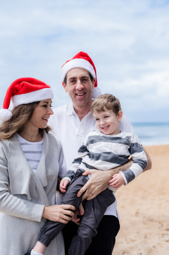 Happy family celebrating Christmas at the beach with Santa hats and joyful expressions - Australian Stock Image