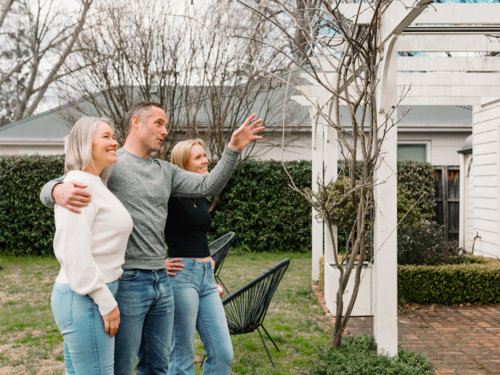 Happy family gathered in the patio of their new home with adult man pointing towards patio rafter - Australian Stock Image