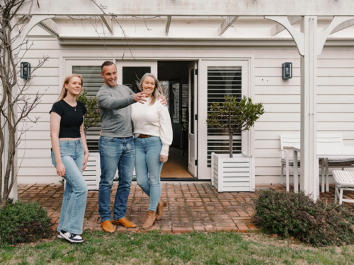 Happy family gathered in the patio of their new home with adult man pointing towards the garden - Australian Stock Image