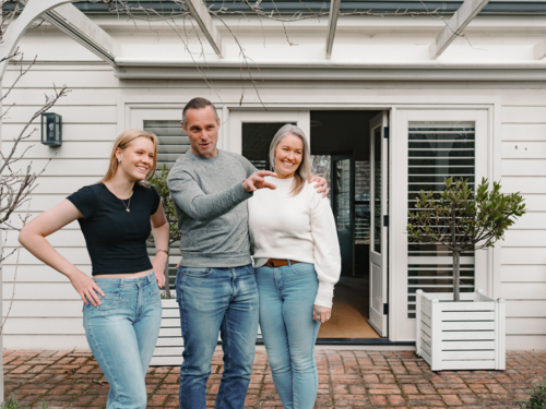 Happy family gathered in the patio of their new home with adult man pointing towards the garden - Australian Stock Image