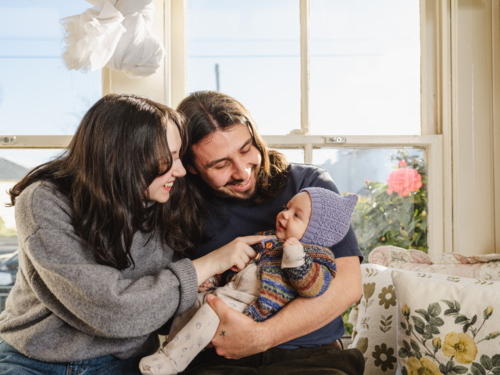 Happy family sitting near windows new parents interacting with baby - Australian Stock Image