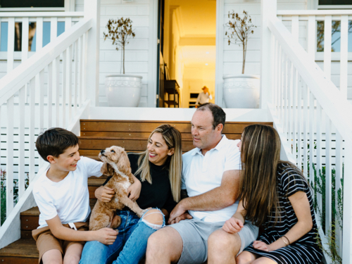 Happy family sitting outside on the steps of their house. - Australian Stock Image