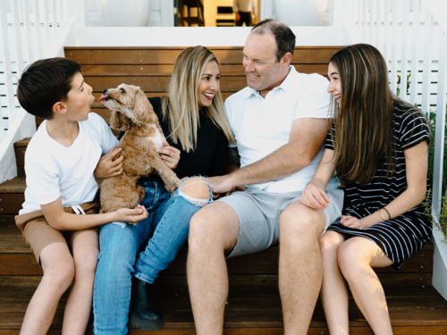 Happy family sitting outside on the steps of their house. - Australian Stock Image