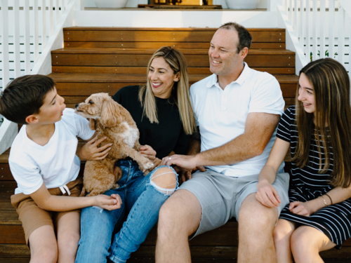Happy family sitting outside on the steps of their house. - Australian Stock Image