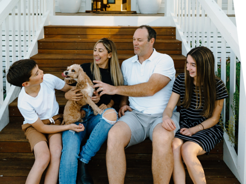 Happy family sitting outside on the steps of their house. - Australian Stock Image