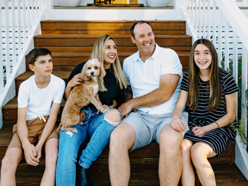 Happy family sitting outside on the steps of their house. - Australian Stock Image