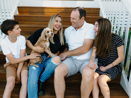 Happy family sitting outside on the steps of their house. - Australian Stock Image
