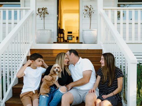 Happy family sitting outside on the steps of their house. - Australian Stock Image