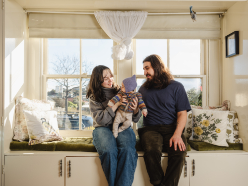 Happy family sitting together near windows inside brightly lit home - Australian Stock Image