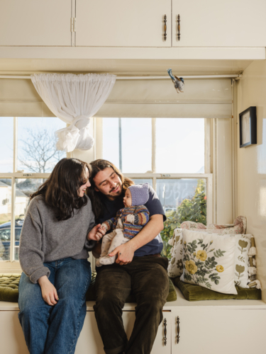 Happy family sitting together near windows inside brightly lit home - Australian Stock Image