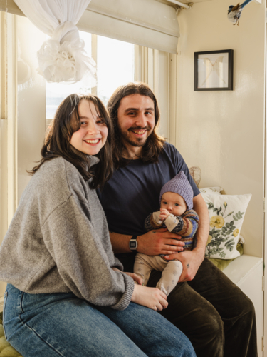 Happy family sitting together near windows inside brightly lit home - Australian Stock Image