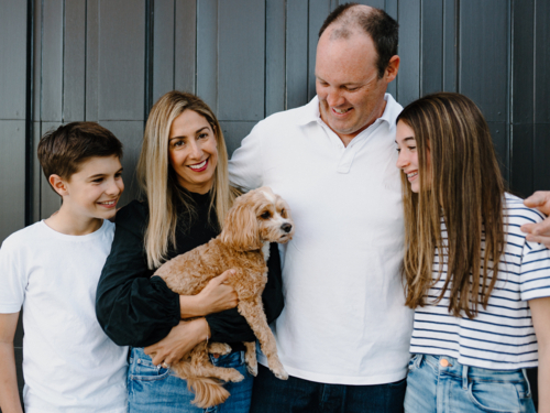 Happy family standing outside home in front of  black garage door - Australian Stock Image