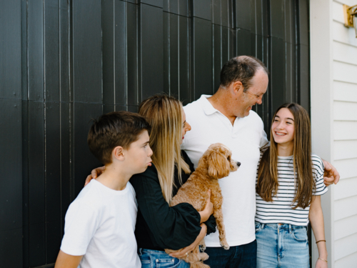 Happy family standing outside in front of black garage door - Australian Stock Image